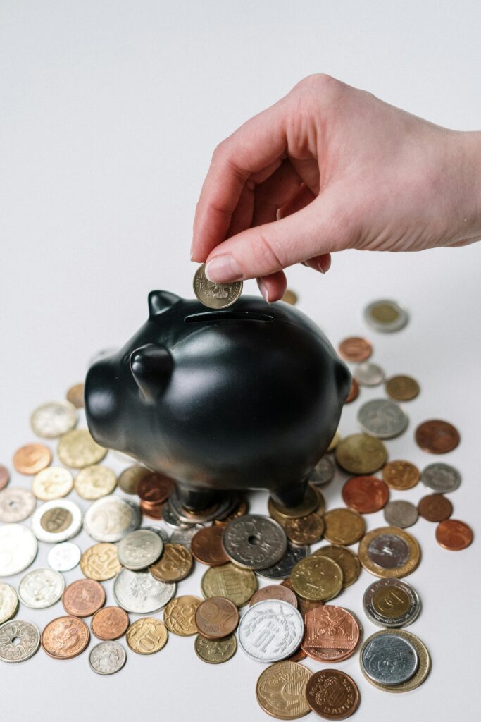 pexels photo 3943723 3943723 Hand inserting coin into a black piggy bank surrounded by various coins, symbolizing savings.