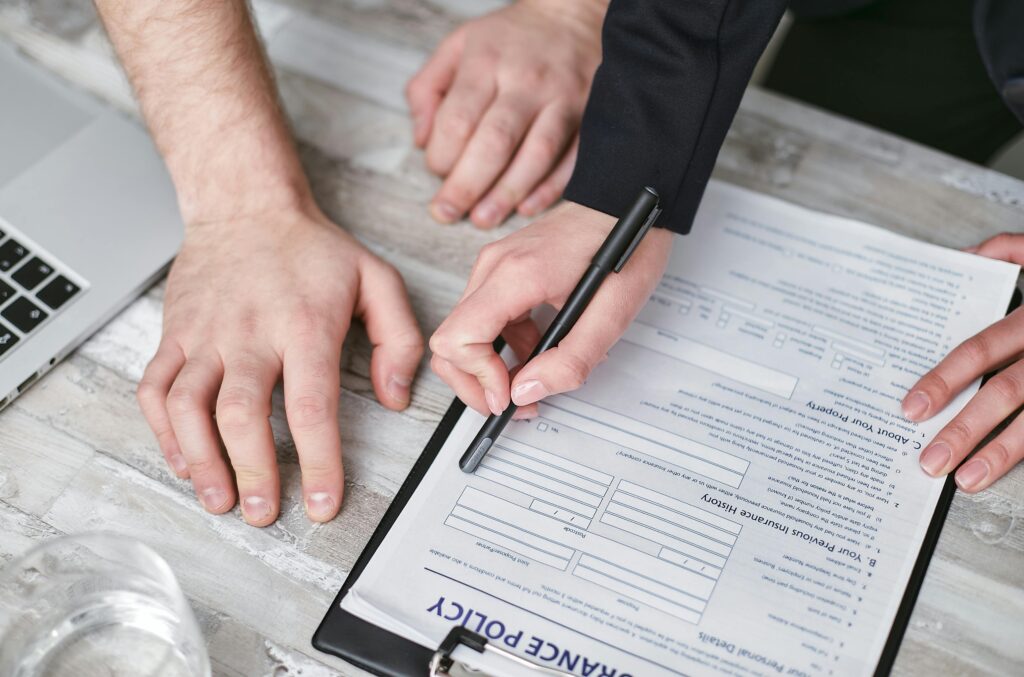 Close-up image of two people signing an insurance policy document on a wooden desk.
